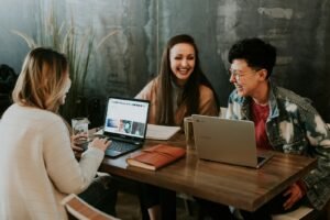 tres personas sentadas frente a la mesa riendo juntas - elegir agencia digital